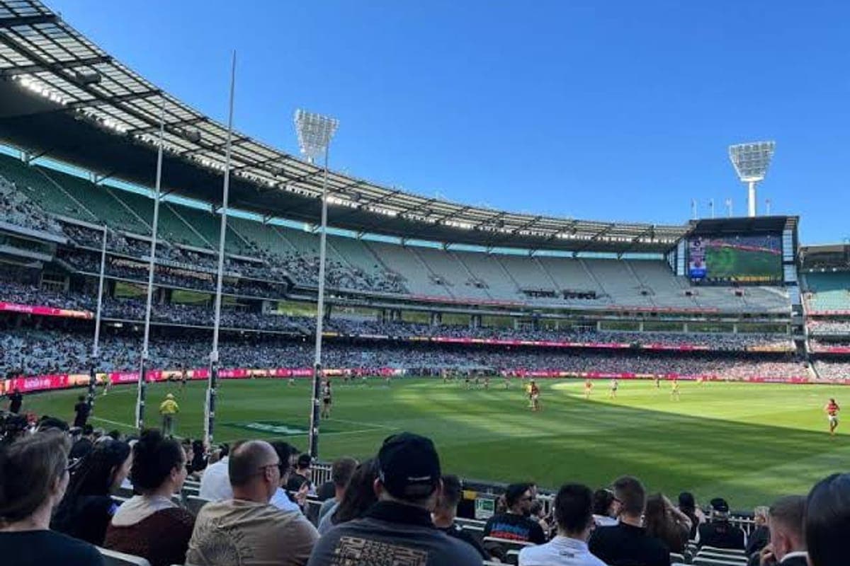 A large crowd watching an Australian rules football match at a stadium on a sunny afternoon