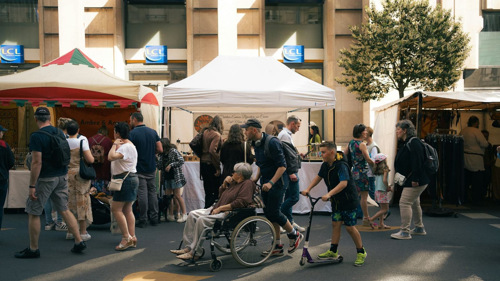 A man pushing an older woman in a wheelchair through a busy street market between stalls