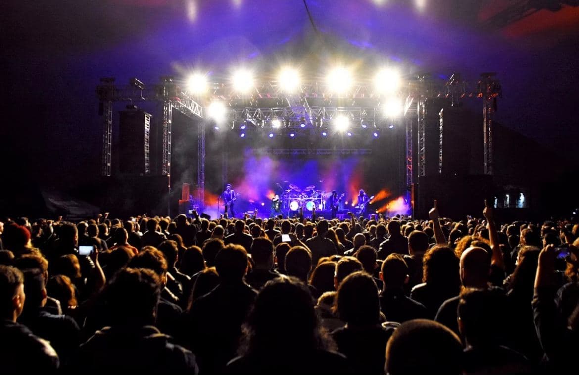 A festival crowd facing a stage lit in deep blue and purple at night