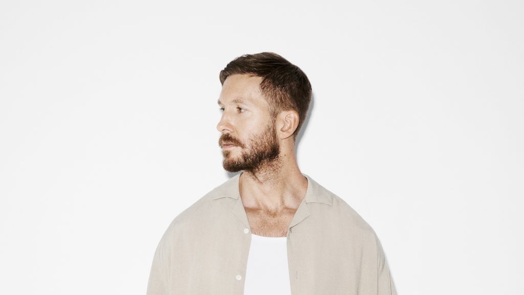 Calvin Harris in a light linen shirt, looking to the side against a plain white background