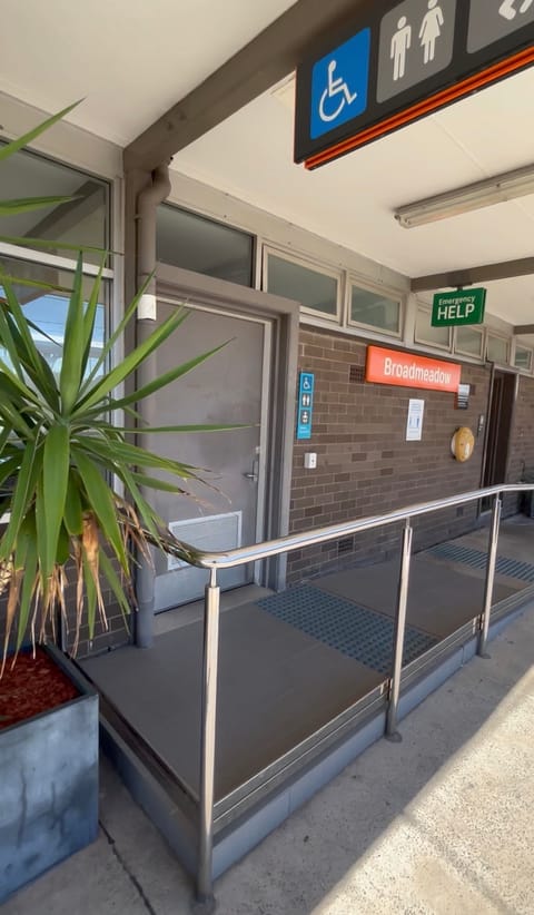 The accessible toilet door at the top of a short ramp with a handrail, beside an Emergency Help sign
