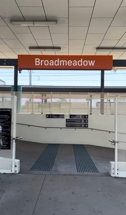 Entrance to Broadmeadow Station under the station sign: a ramp with tactile strips leads down, with signs to Platform 1 for Sydney and Platforms 2 and 3 for Newcastle