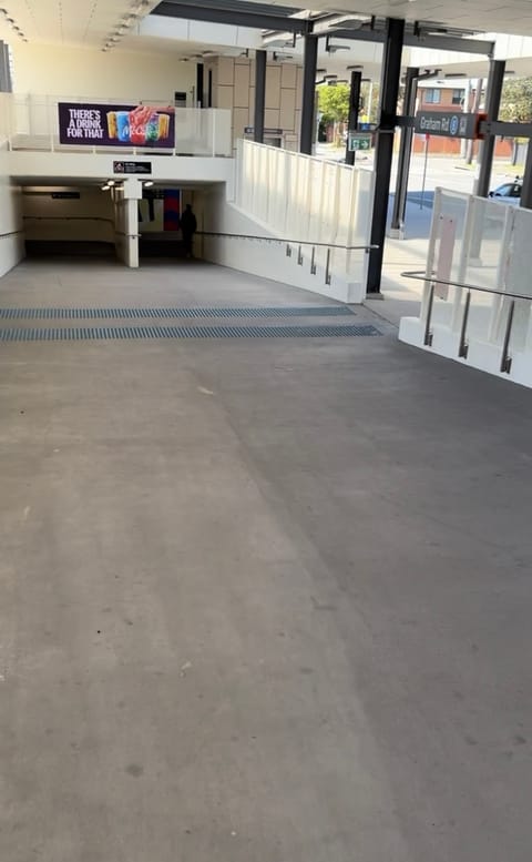 The wide graded ramp down to the station underpass, with handrails and tactile strips, beside the Graham Rd exit