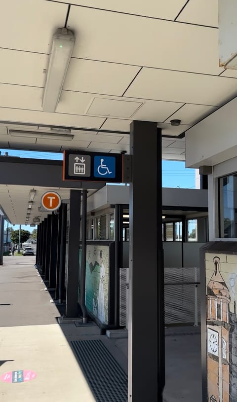 The station entrance from the street, with lift and wheelchair signs, the orange T train sign, and tactile tiles on the path
